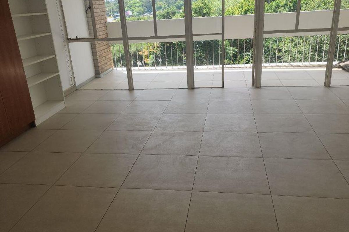 Spacious, light-filled living area featuring neutral floor tiles, built-in shelving, and large glass doors opening onto a balcony with scenic views.