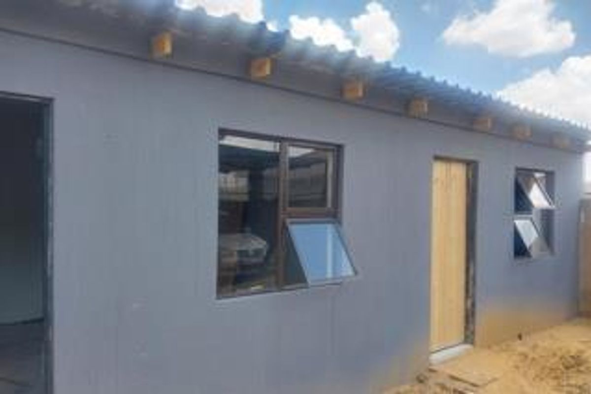Exterior view of a modern grey-painted dwelling featuring aluminium window frames and a corrugated roof structure.