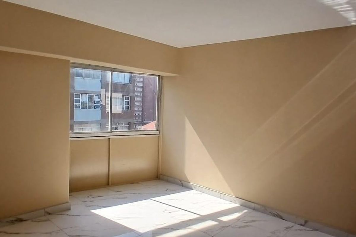 A bright, empty bedroom featuring modern marble-look floor tiles and a large sliding window allowing for ample natural light.