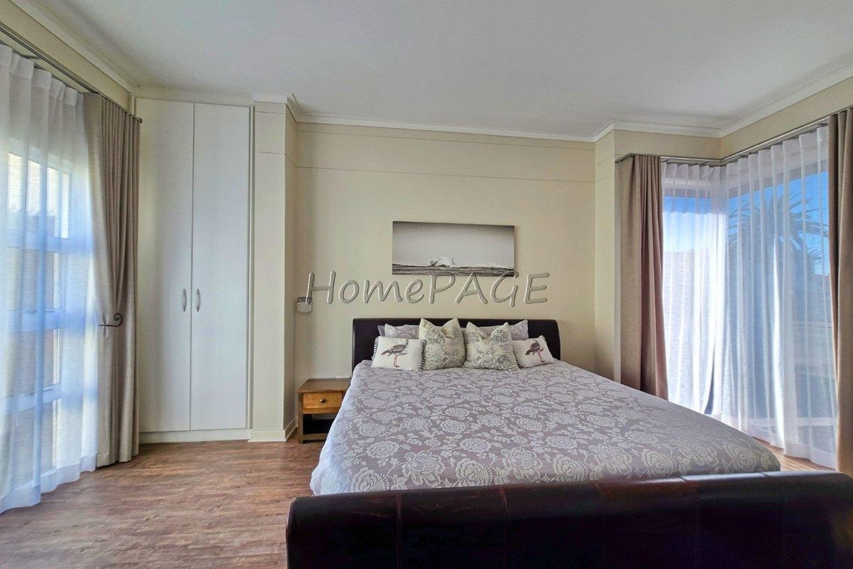 A well-lit bedroom featuring built-in cupboards, wood-look flooring, and large windows with curtains, offering a comfortable and functional living space.