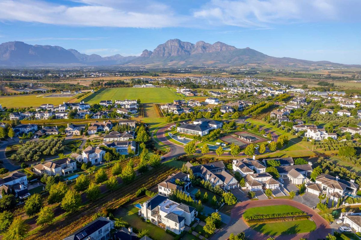 An aerial view of a well-maintained residential estate featuring landscaped grounds, paved roads, and mountain views in the background.
