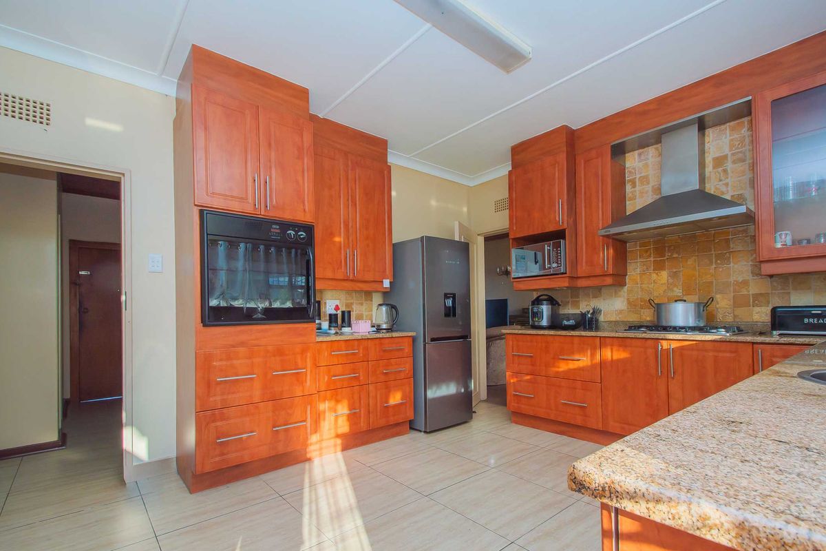A well-maintained kitchen featuring warm-toned wooden cabinetry, granite countertops, a built-in oven, and a stainless steel extractor fan with a tiled backsplash.