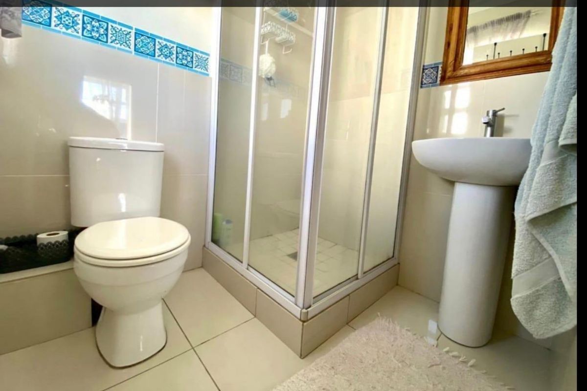 A functional bathroom featuring a pedestal basin, a corner shower enclosure, and a toilet with decorative wall tile accents.