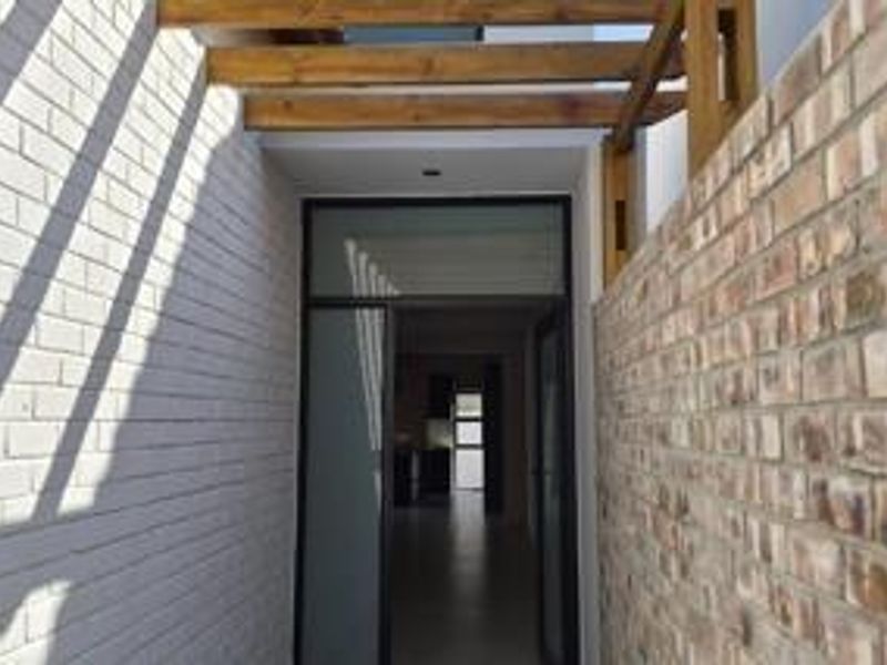 A modern entrance featuring a timber pergola, contrasting painted and exposed brick walls, and a glass panel door leading into the home.