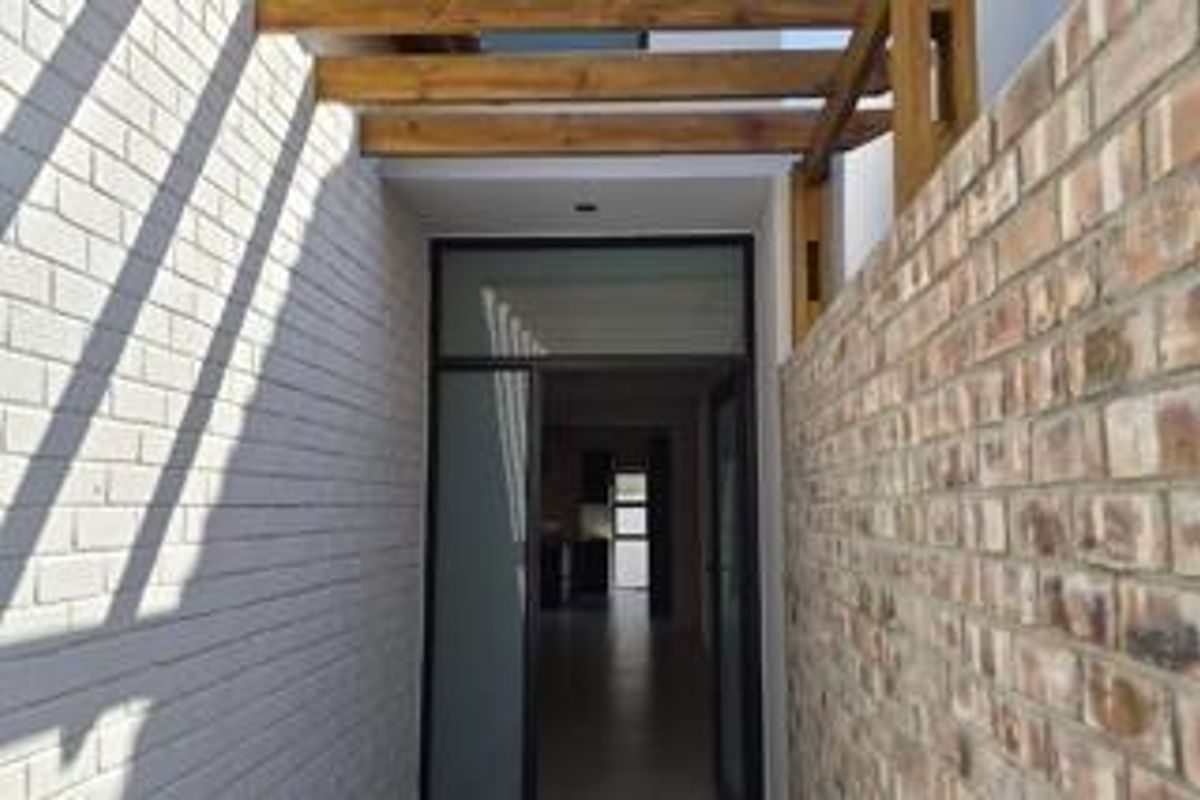 A modern entrance featuring a timber pergola, contrasting painted and exposed brick walls, and a glass panel door leading into the home.