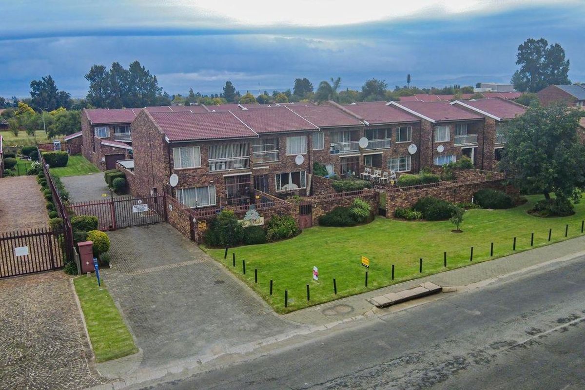 Aerial view of a residential cluster complex featuring face-brick townhouses with tiled roofs, paved driveways, and communal garden areas.