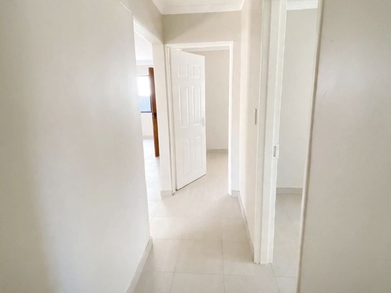A bright, neutral hallway featuring clean tiled flooring and multiple doorways leading to adjacent rooms, providing a seamless flow throughout the home.