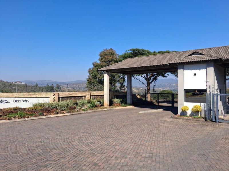 The entrance to the Bikki Wes estate features a paved driveway, secure gate access, and a well-maintained brick boundary wall with electric fencing.