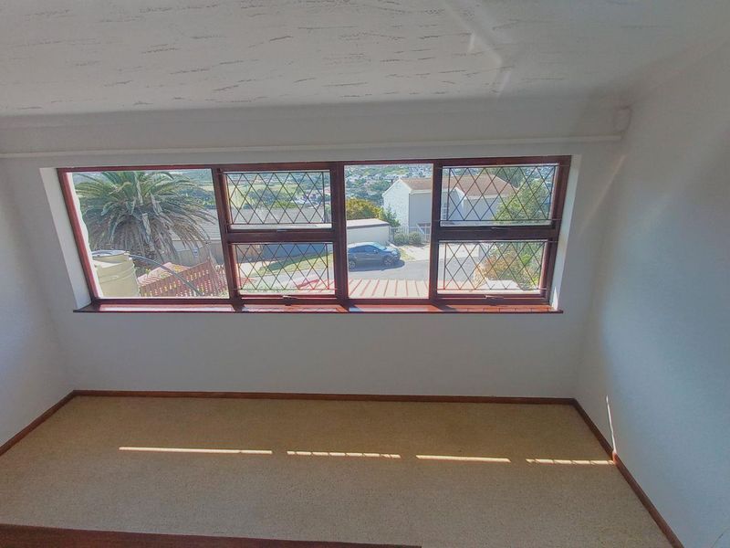 An empty bedroom featuring carpeted flooring and large leaded glass windows with timber frames, offering a view of the surrounding neighborhood.