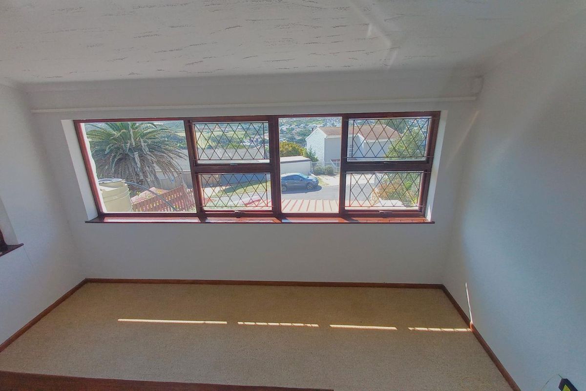 An empty bedroom featuring carpeted flooring and large leaded glass windows with timber frames, offering a view of the surrounding neighborhood.