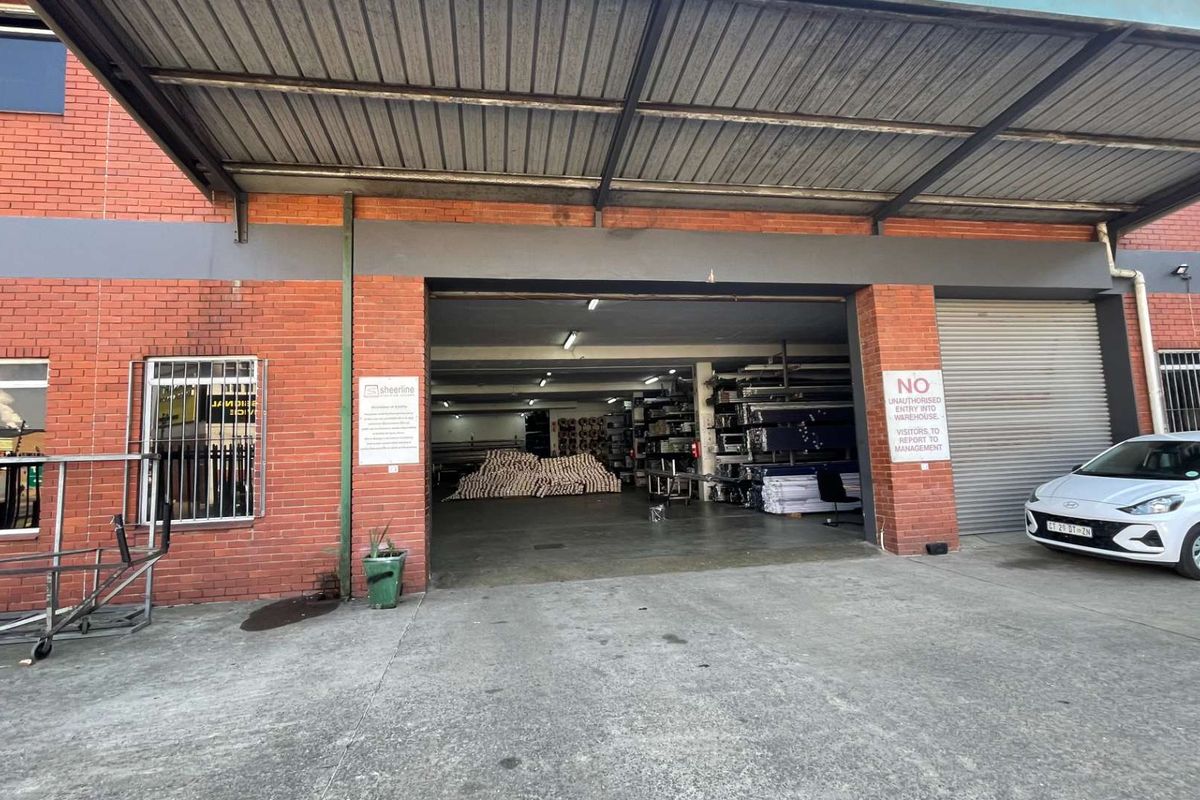 Front exterior view of a commercial warehouse featuring a large covered loading bay, exposed brick facade, and a secure roller shutter entrance.