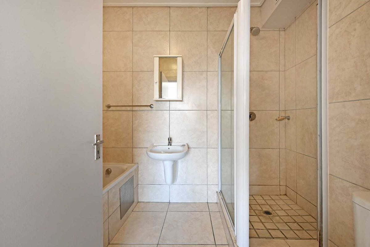 A functional bathroom featuring a pedestal basin, a built-in bathtub, and a separate glass-enclosed shower with neutral wall and floor tiling.