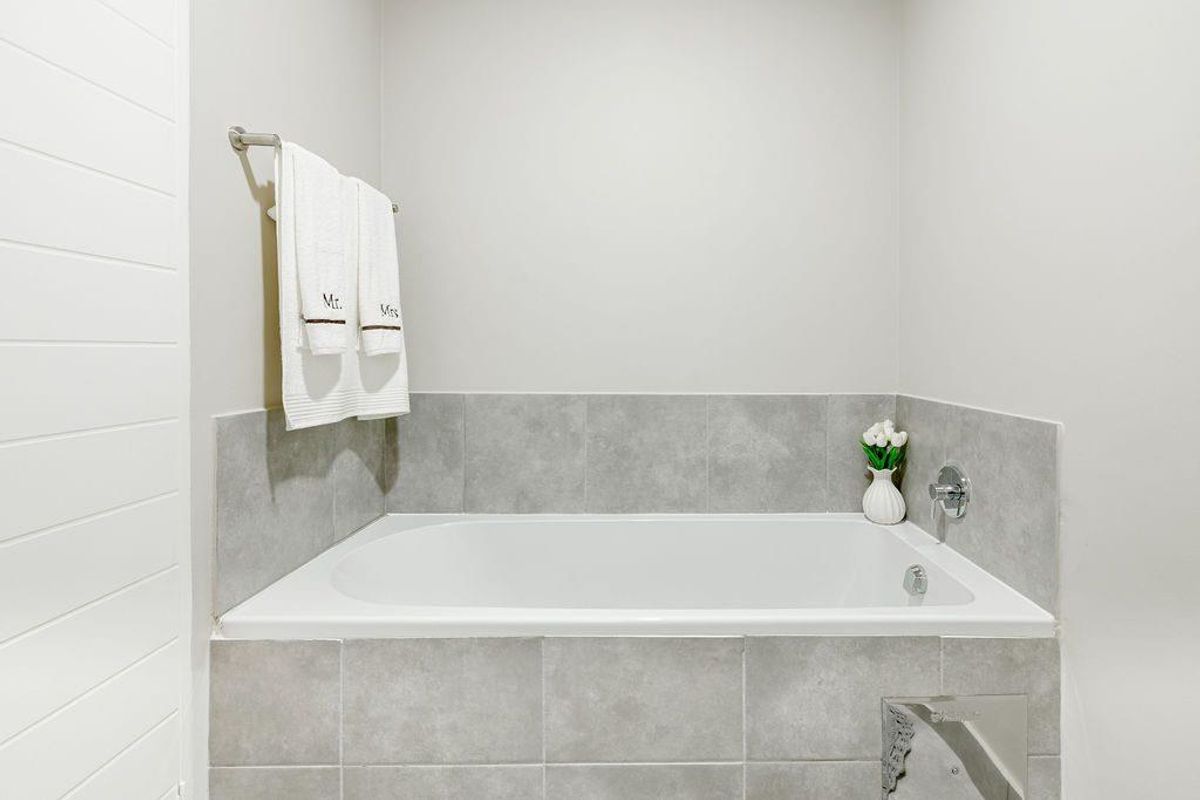A clean and modern bathroom featuring a built-in bathtub with neutral grey tiled surround and chrome fixtures.