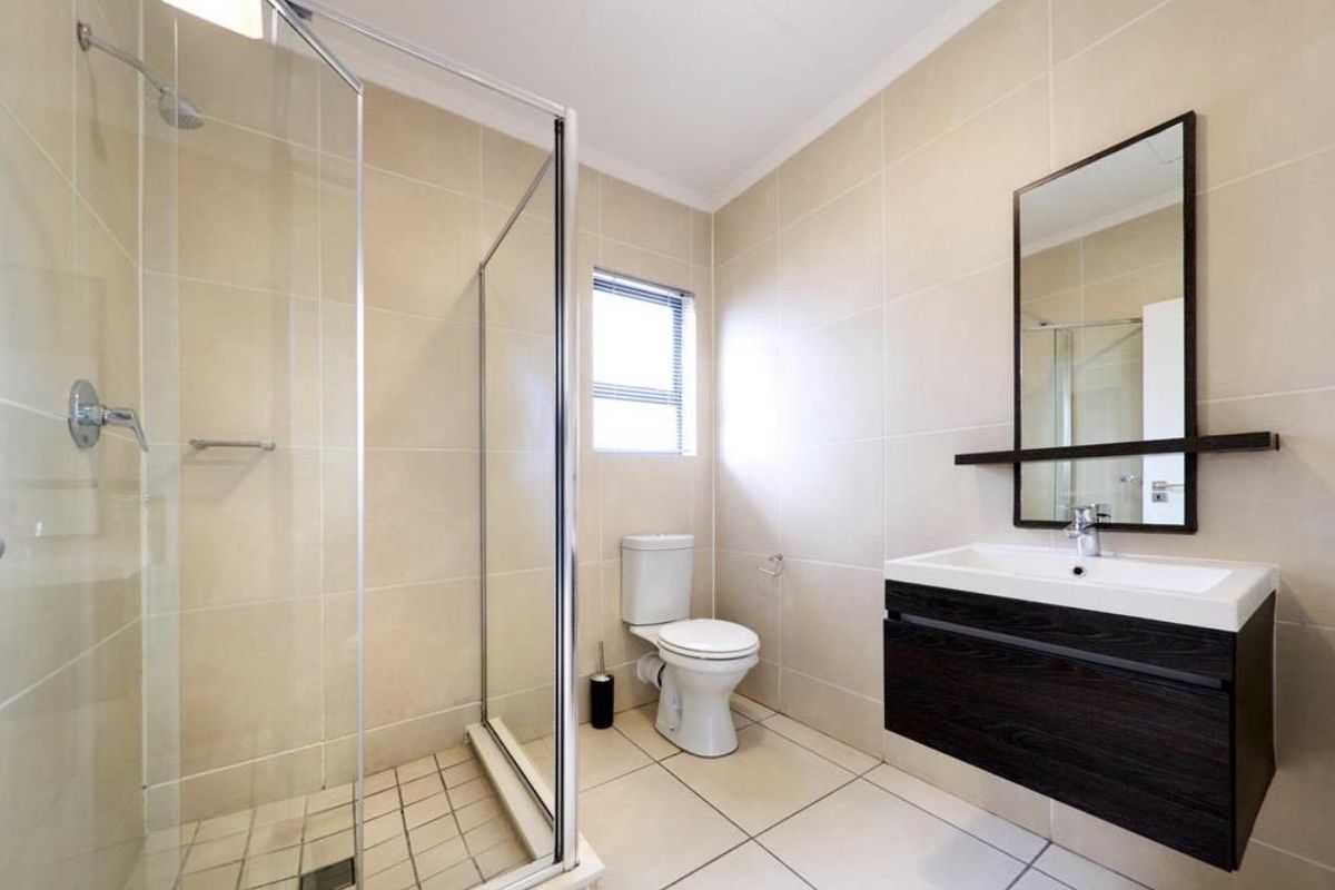 Modern bathroom featuring a glass-enclosed shower, wall-mounted vanity with basin, and a toilet, finished with neutral floor-to-ceiling tiling.