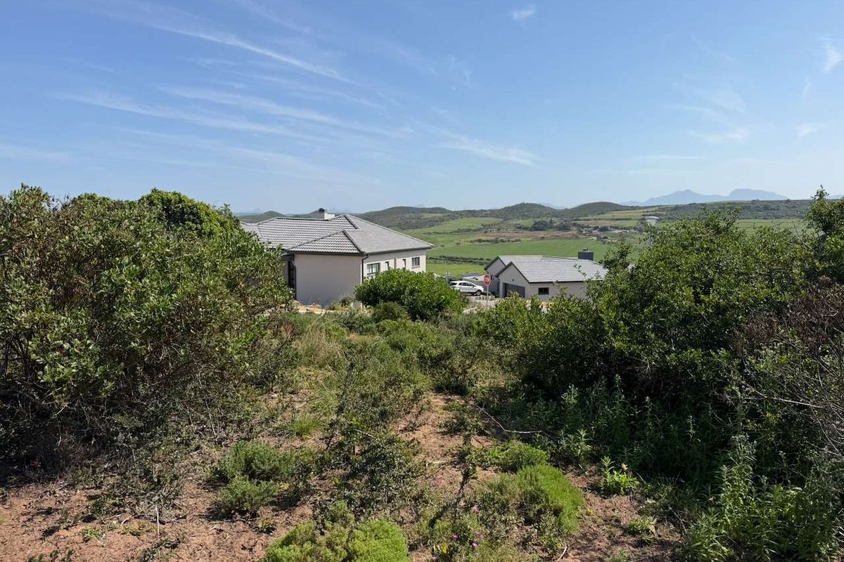 A view of the vacant residential land featuring natural vegetation and a sloped landscape with surrounding neighborhood homes in the distance.