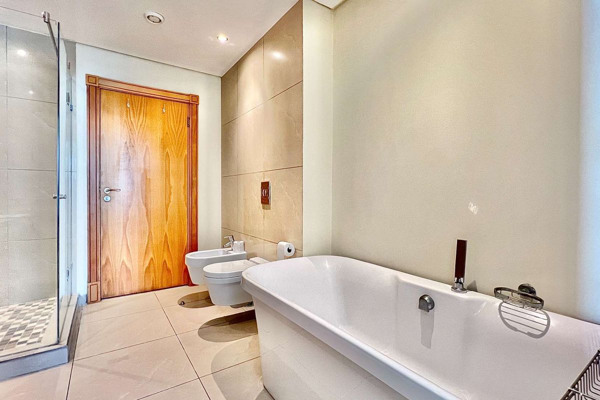 Modern bathroom featuring a freestanding bathtub, glass-enclosed shower, wall-mounted bidet and toilet, and neutral floor-to-ceiling tiling.