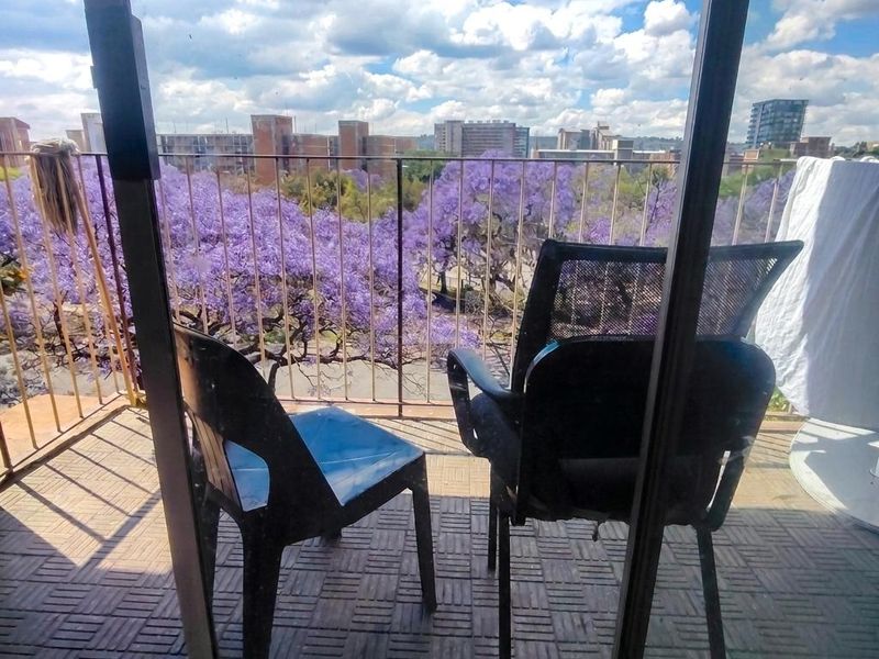 A balcony featuring tiled flooring and a metal railing, offering an elevated view of the surrounding neighborhood and flowering trees.