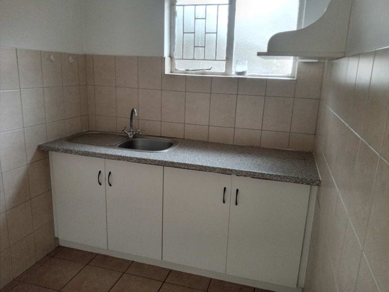 A functional kitchen area featuring built-in cabinetry, a stainless steel sink, tiled backsplash, and tiled flooring, providing a clean and practical workspace.