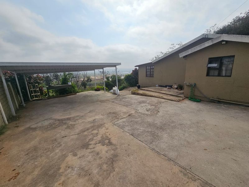 Exterior view of the property featuring a concrete driveway, a covered carport, and visible wear to the building's exterior plaster and paint.