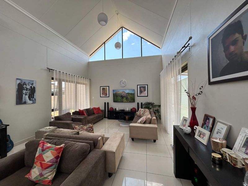 Spacious living room featuring a high vaulted ceiling, large triangular clerestory windows for natural light, and tiled flooring with access to outdoor areas.
