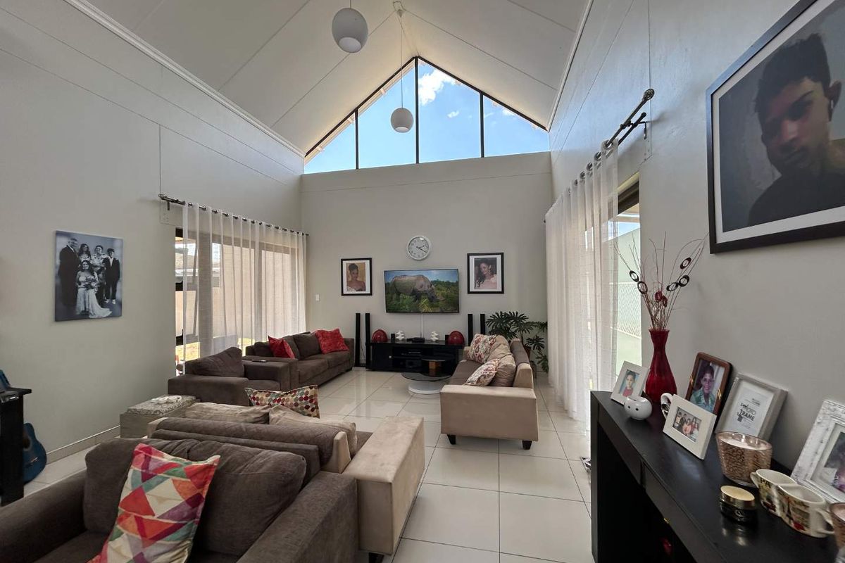 Spacious living room featuring a high vaulted ceiling, large triangular clerestory windows for natural light, and tiled flooring with access to outdoor areas.