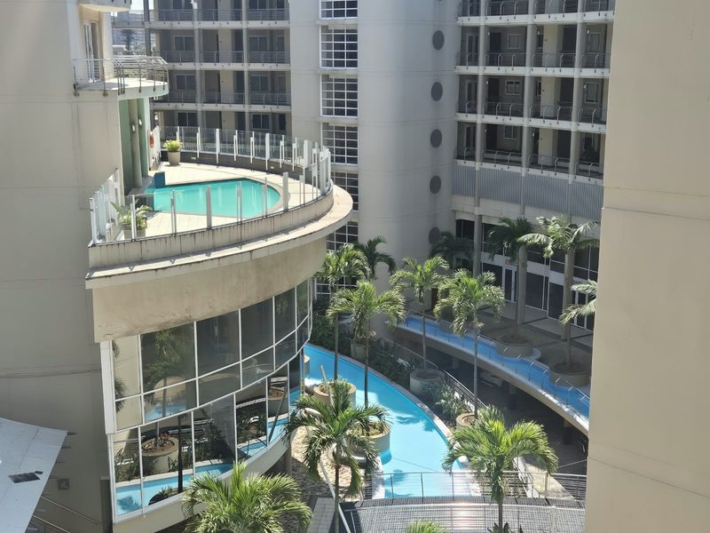 An elevated view of the apartment complex featuring a swimming pool, landscaped garden areas, and modern architectural design with glass balustrades.