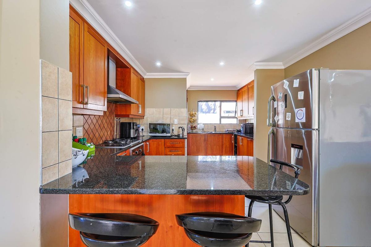 A functional kitchen featuring wooden cabinetry, granite countertops, a breakfast bar, and integrated stainless steel appliances.