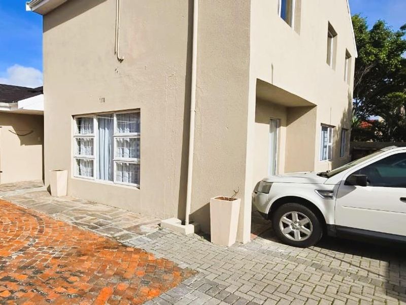 Front exterior view of the apartment building featuring brick paved driveway, security gate, and casement windows.
