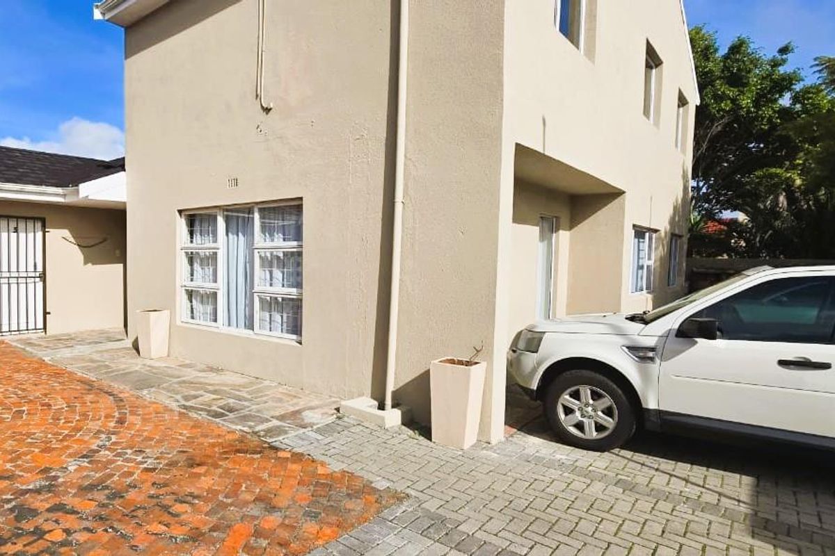 Front exterior view of the apartment building featuring brick paved driveway, security gate, and casement windows.