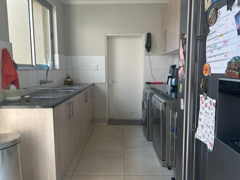 A functional laundry room featuring built-in cabinetry, granite countertops, a stainless steel sink, and tiled flooring with space for appliances.