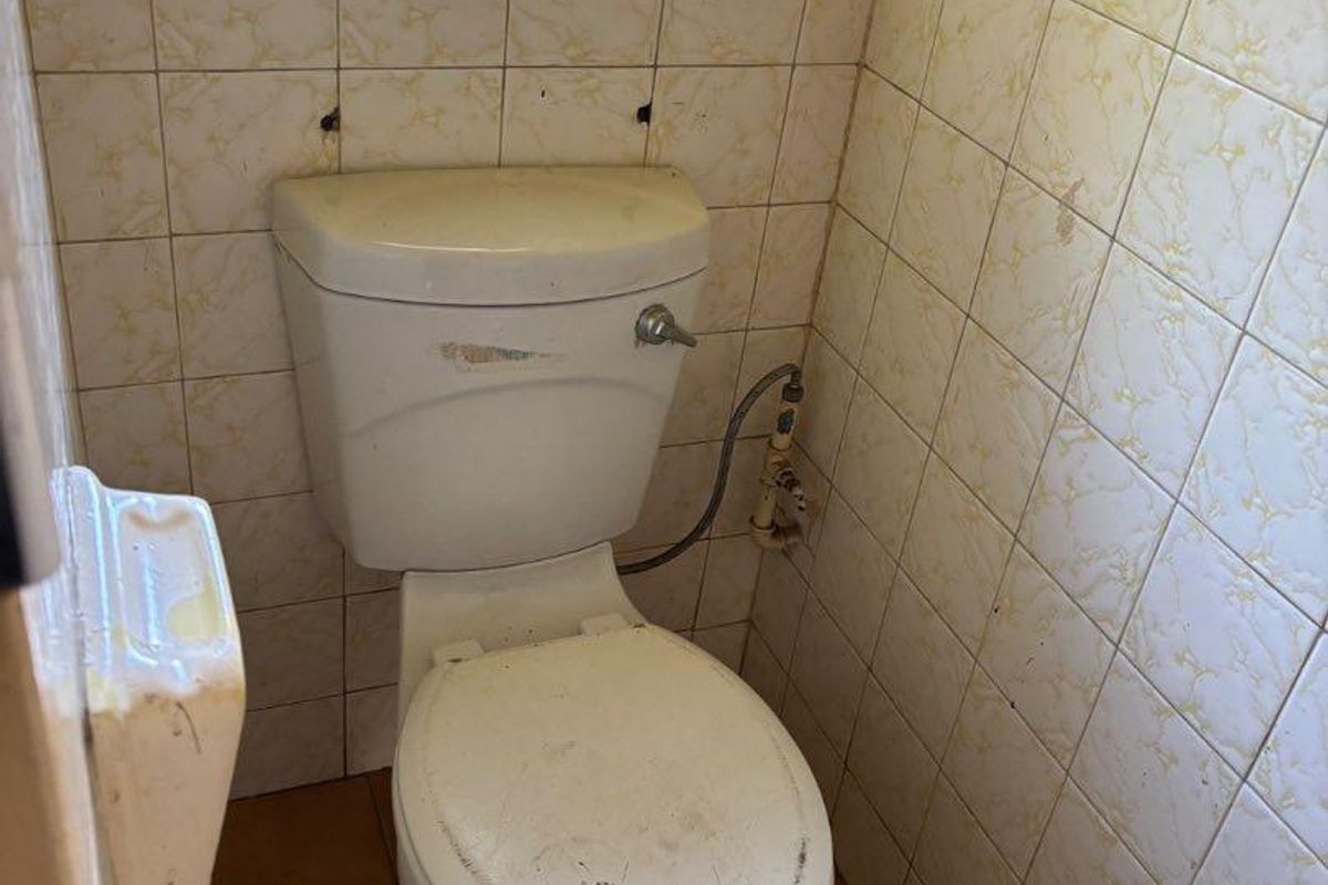 A small, dated bathroom featuring a standard toilet, tiled walls and flooring, and an obscured glass window.