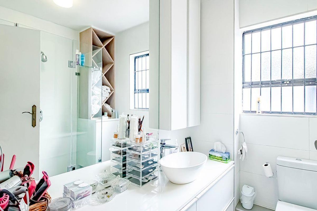 A bright, modern bathroom featuring a vessel sink vanity, glass-enclosed shower, built-in shelving, and a window with security bars.