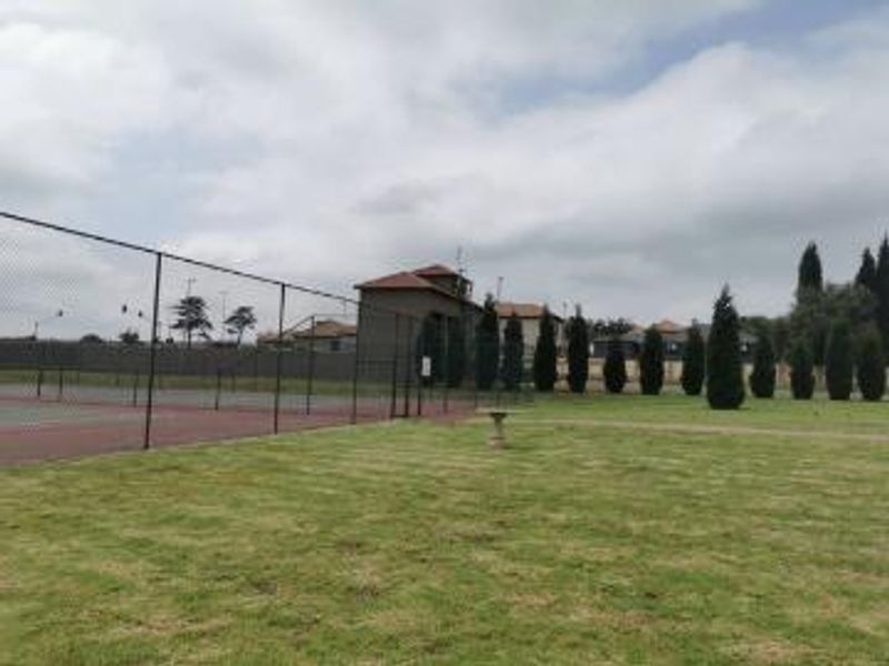A well-maintained communal tennis court facility featuring chain link fencing and surrounding landscaped lawn areas within the apartment complex grounds.