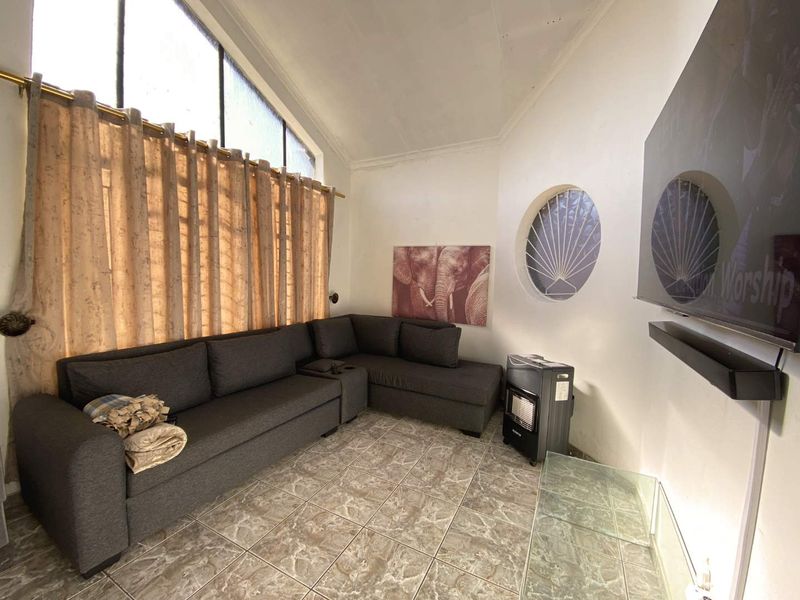 Living room featuring tiled flooring, a vaulted ceiling, and unique architectural windows, including a circular feature window and a large raked window.