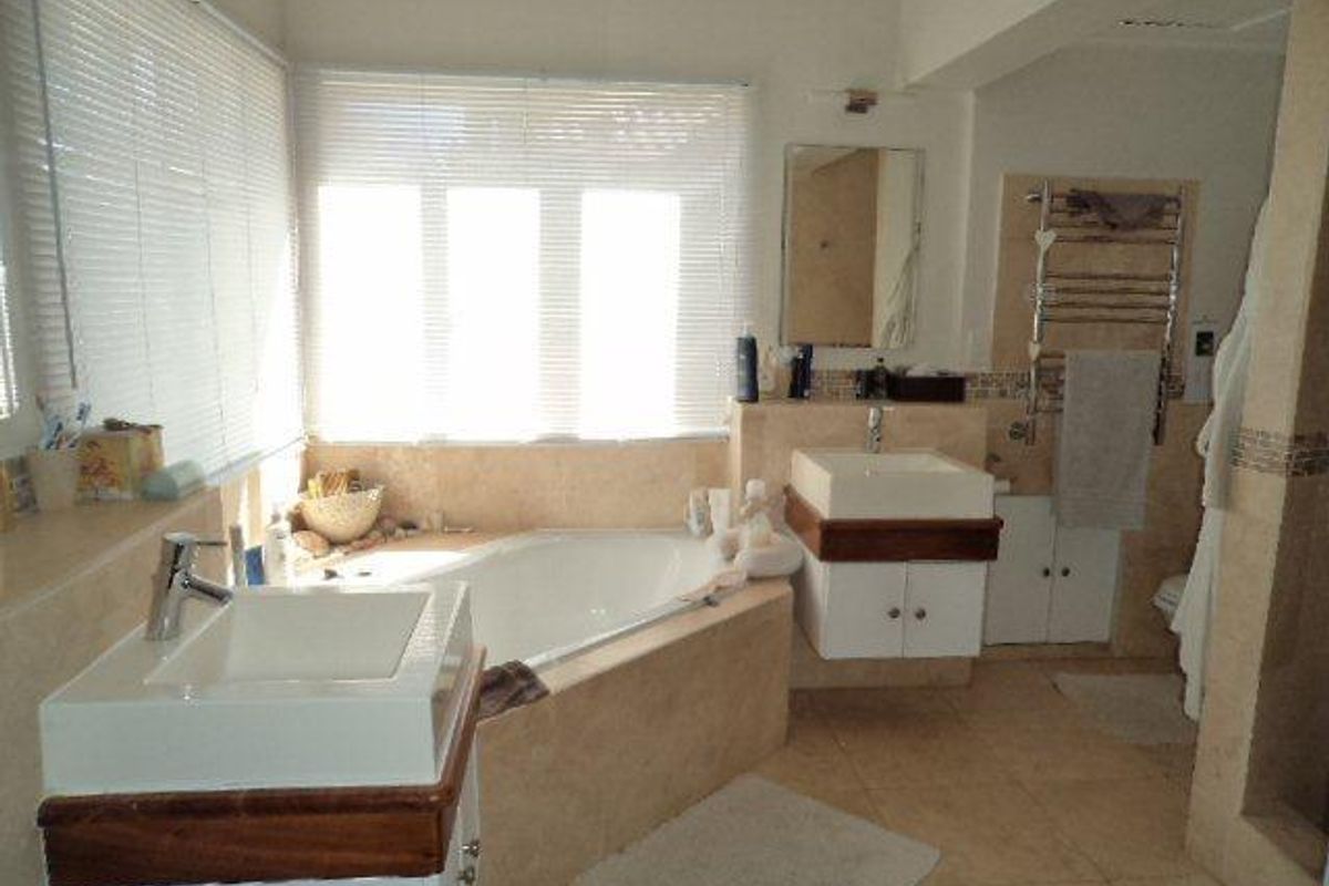 A spacious bathroom featuring a corner bathtub, dual vanity basins with timber detailing, and a wall-mounted heated towel rail.