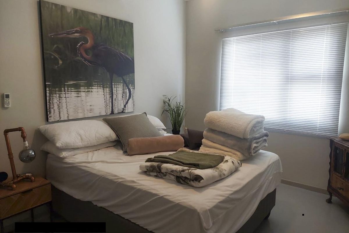 A well-maintained bedroom featuring tiled flooring, a wall-mounted air conditioning unit, and venetian blinds for privacy.