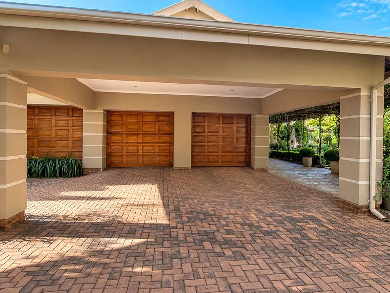 A well-maintained double garage with wooden doors and a spacious paved driveway under a covered carport structure.