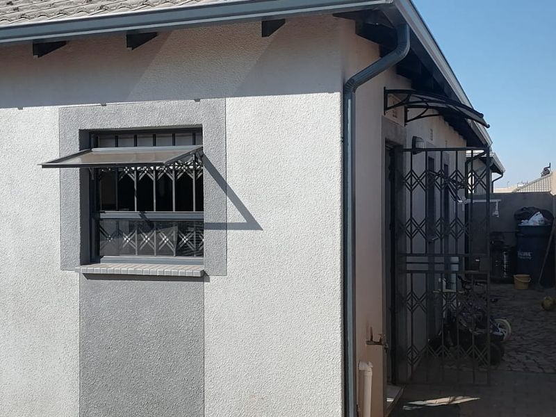 Rear exterior view of the property featuring security gates, security bars on windows, tiled roof, and a paved side walkway.