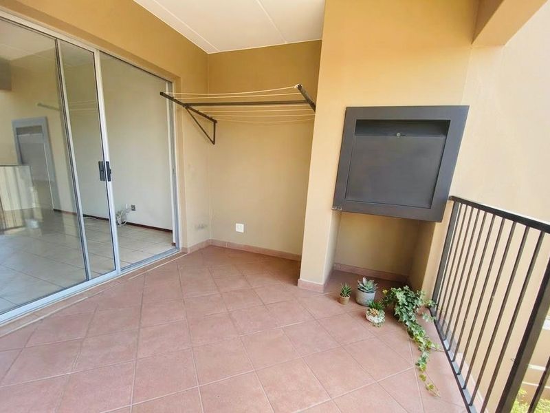 A covered balcony featuring tiled flooring, a built-in braai, and a metal balustrade, providing an ideal space for outdoor relaxation.