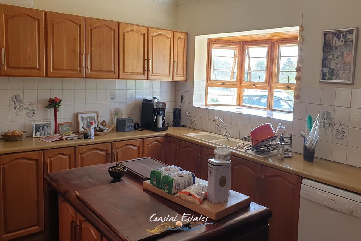 A functional kitchen featuring traditional wooden cabinetry, laminate countertops, a double basin sink, and a tiled backsplash with natural light from the window.