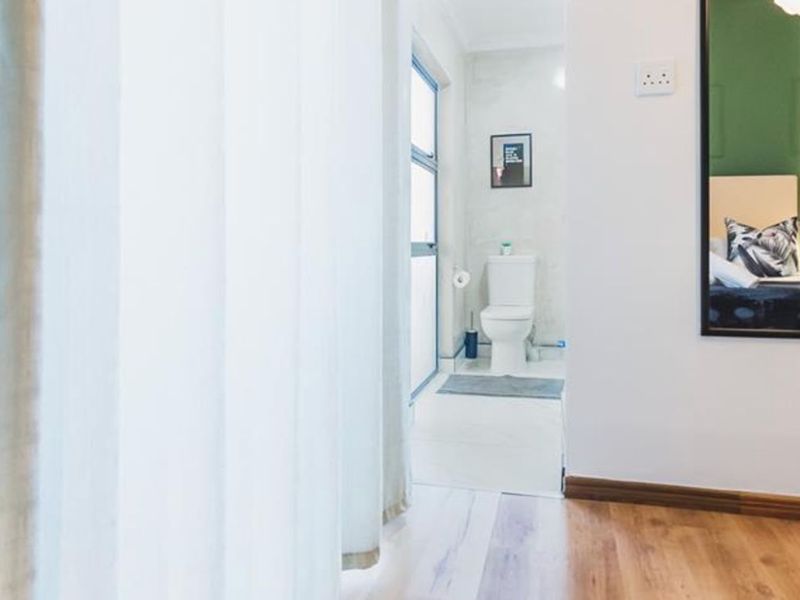 A view into a functional bathroom featuring a toilet and clean finishes, viewed from an adjacent room with laminate flooring.