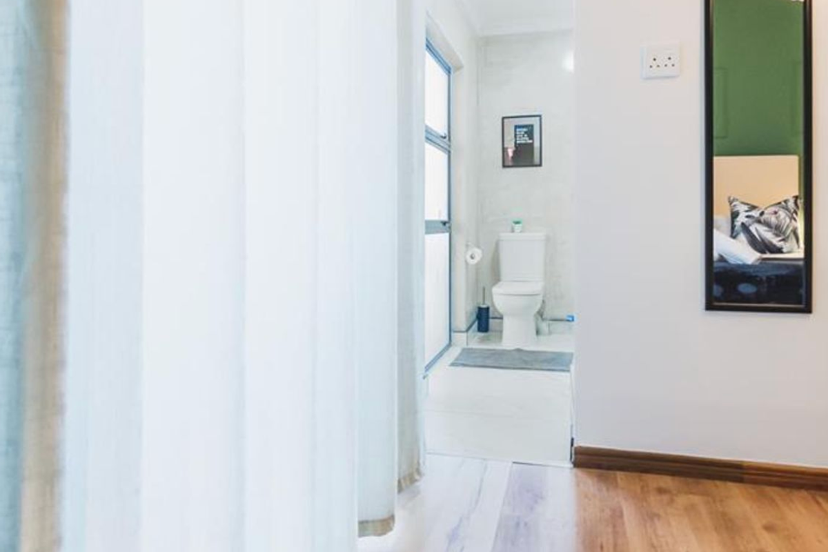A view into a functional bathroom featuring a toilet and clean finishes, viewed from an adjacent room with laminate flooring.