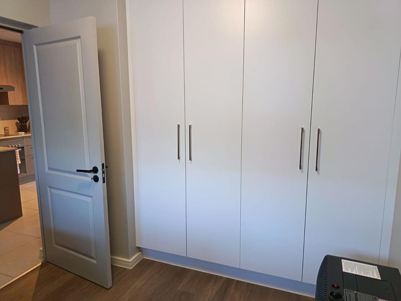 A clean, modern bedroom featuring neutral walls, laminate flooring, and ample built-in cupboard storage space.