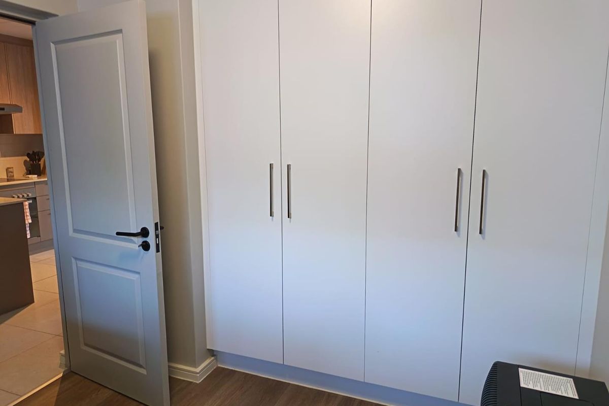 A clean, modern bedroom featuring neutral walls, laminate flooring, and ample built-in cupboard storage space.