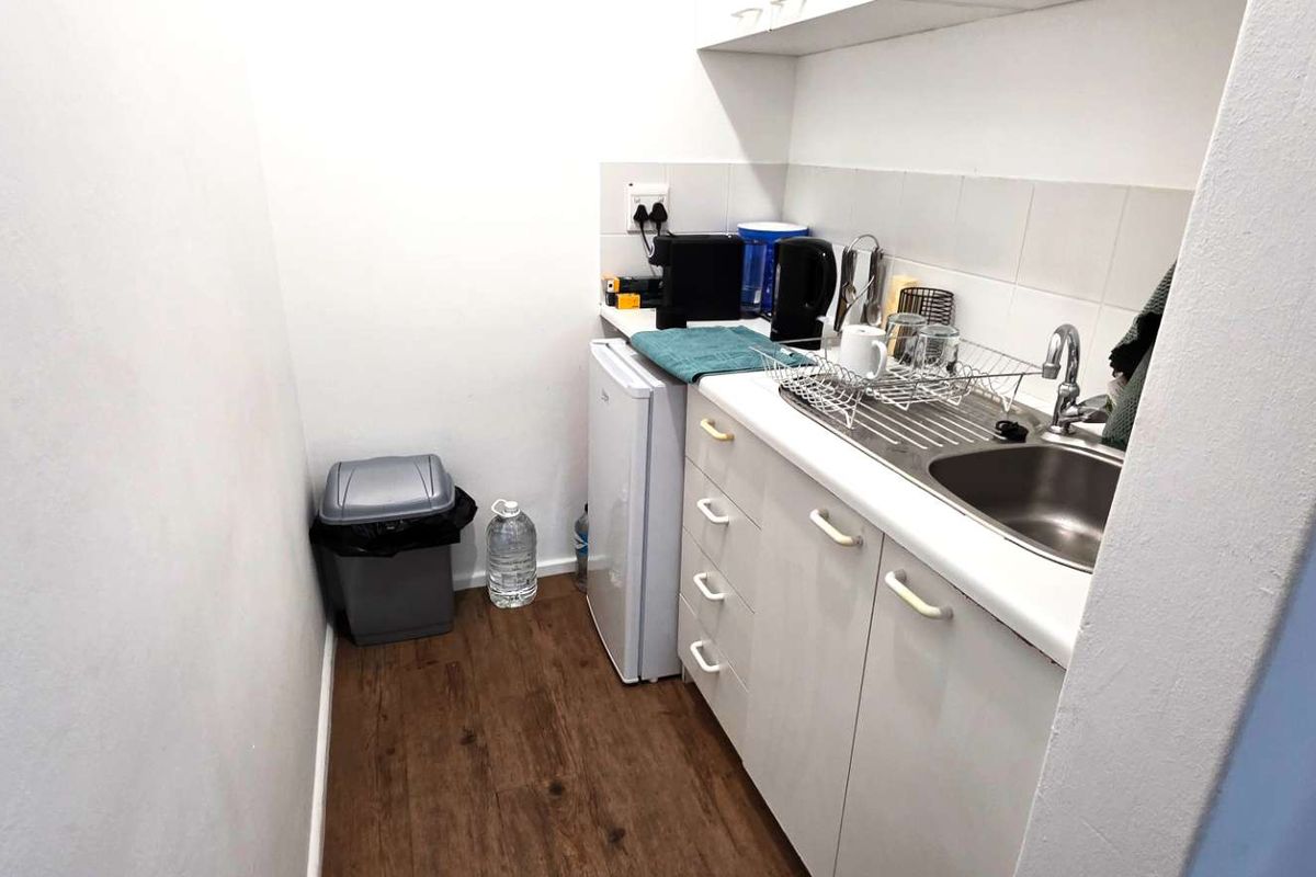 A compact kitchenette area featuring built-in cabinetry, a stainless steel sink, and a tiled backsplash, suitable for office utility use.