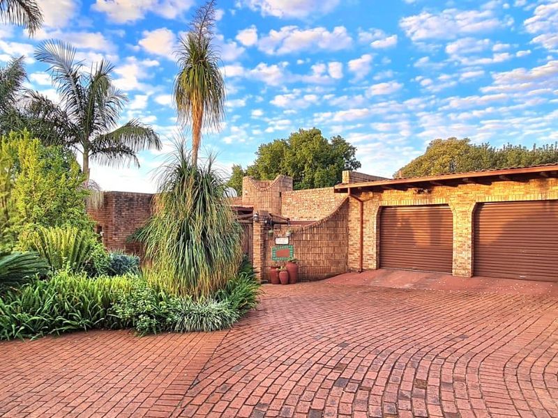 Front view of the property featuring a brick driveway, established garden, and a double garage with roller shutter doors.