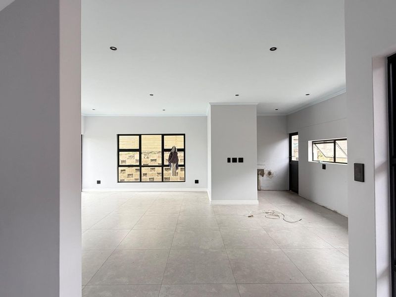 Spacious, light-filled open-plan living area featuring modern tiled flooring, recessed downlights, and sleek black aluminium window frames in a neutral, contemporary setting.
