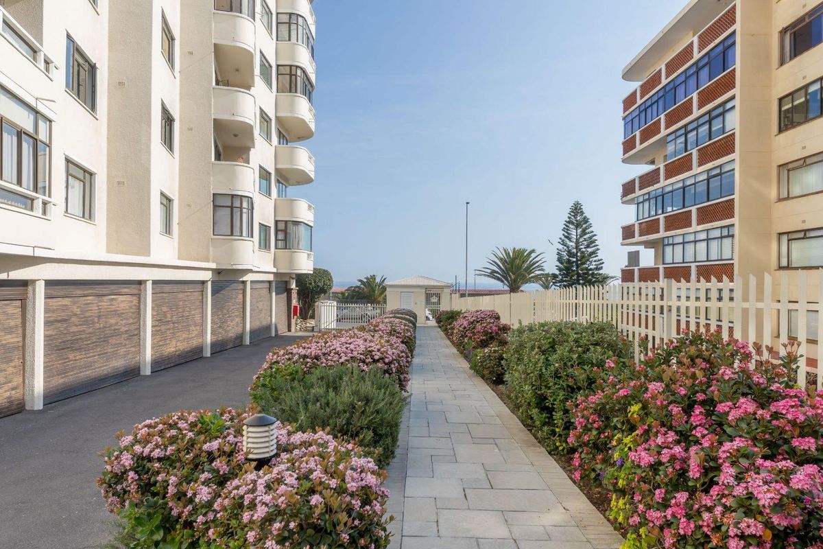 A well-maintained exterior pathway between apartment buildings, featuring paved walkways, manicured garden beds, and secure garage access.