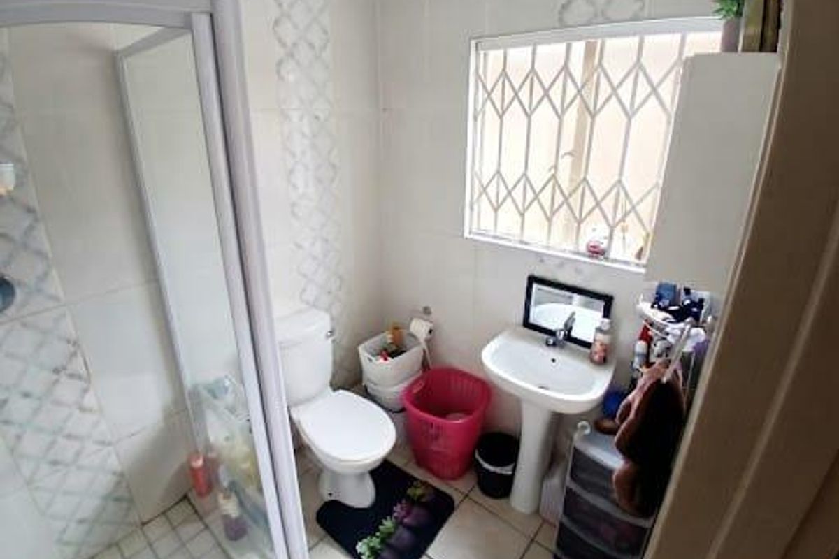 A functional bathroom featuring a shower enclosure, pedestal basin, and toilet, with tiled finishes and a security gate on the window.