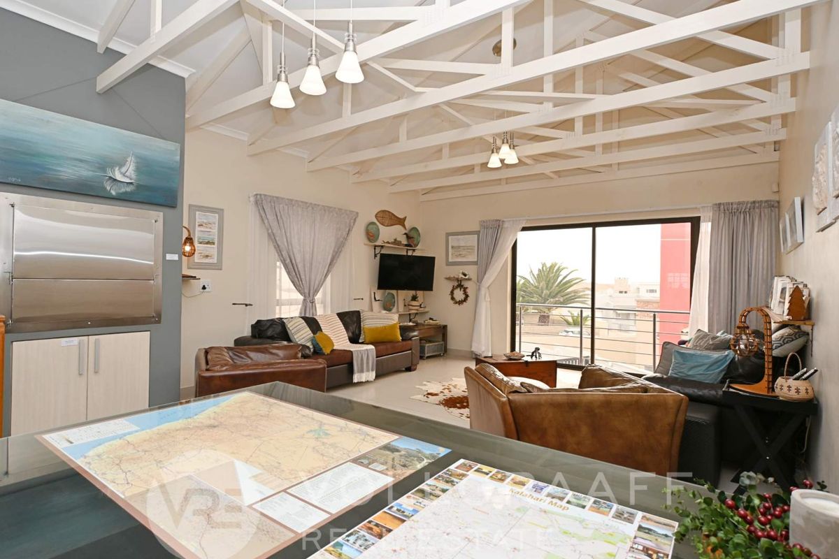 Spacious living area featuring high vaulted ceilings with exposed timber trusses, a built-in stainless steel braai, and large sliding doors leading to a balcony.